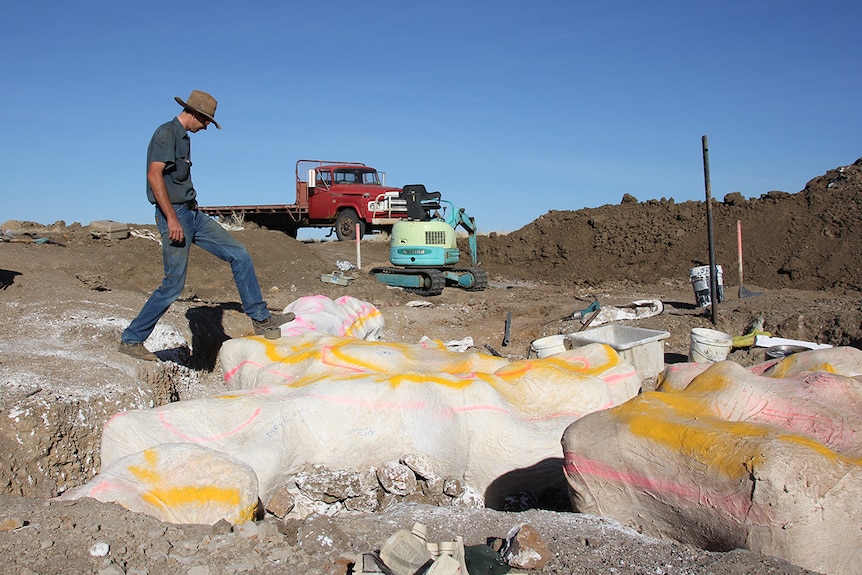 Bob Elliott leans his foot onto a dinosaur bone dug out of the ground at Winton property