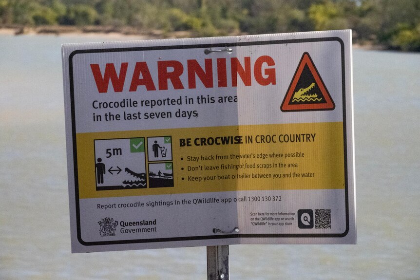 A sign in front of a creek, warning that a crocodile has been spotted recently and people should stay away from the water's edge