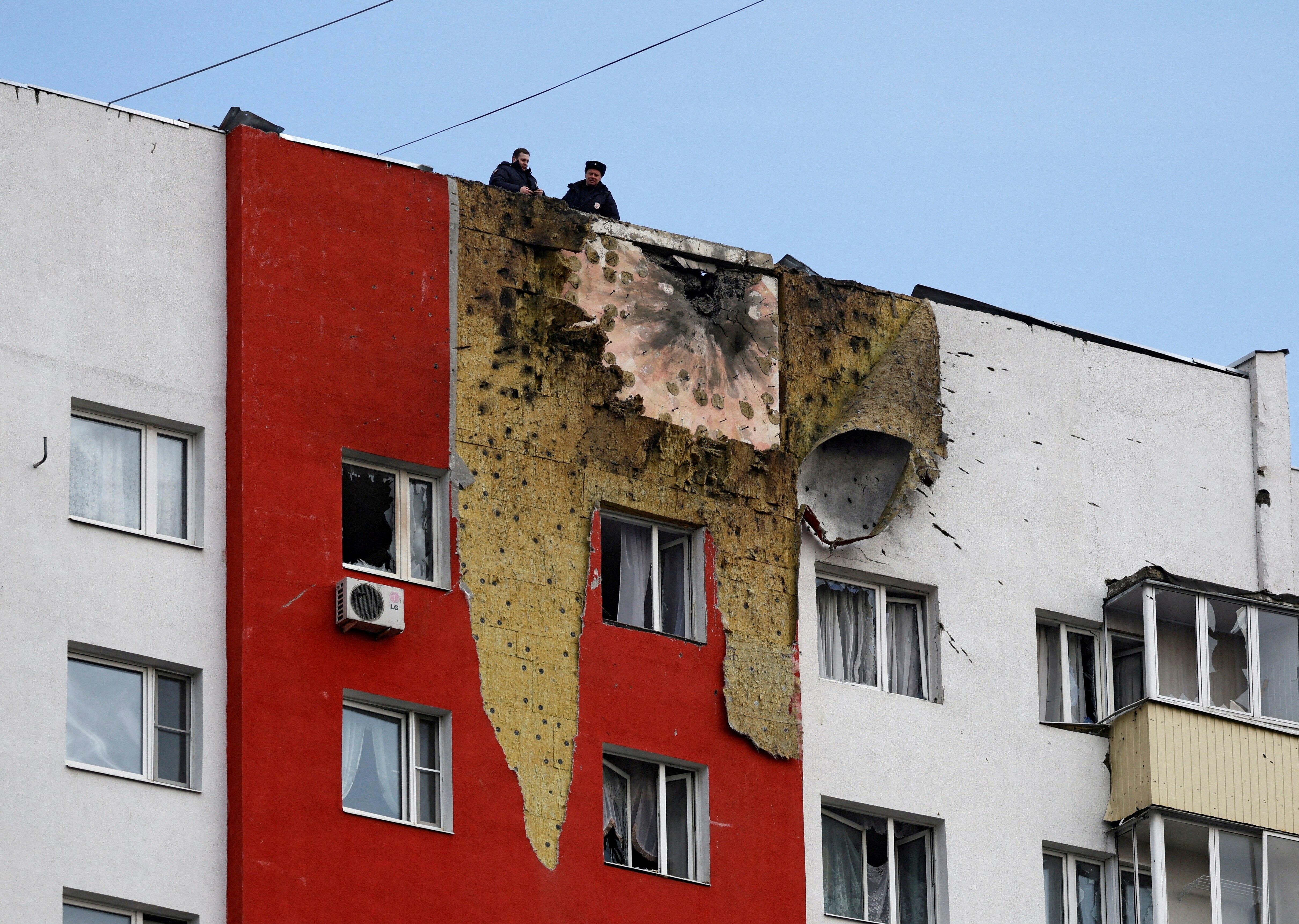 Two police officers in black clothes standing on the roof of a red and white apartment block with a large explosion mark