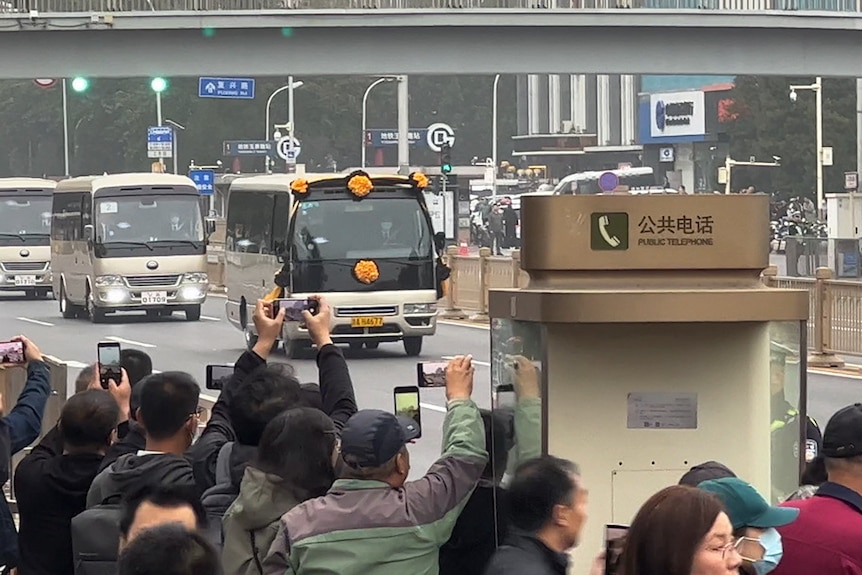 a decorated van driving down a highway as crowds of people hold up smartphone cameras to film