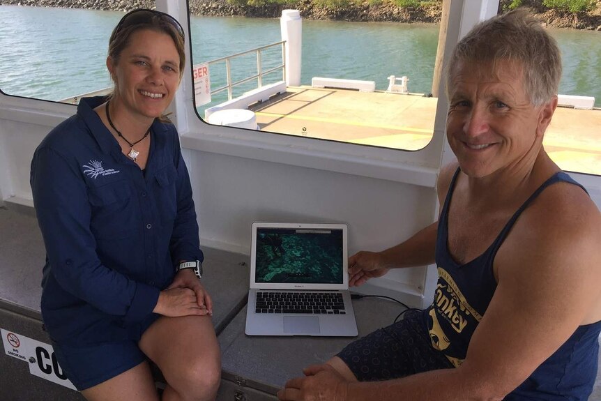 A woman and man sit on either side of a laptop, which has pictures of crown-of-thorns starfish.