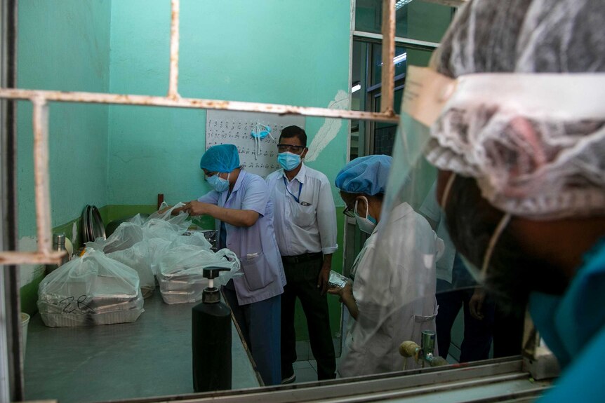 Hospital workers in scrubs sort through bags of aluminium meal boxes