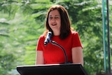 Annastacia Palaszczuk in front of a microphone speaking at GOMA with greenery in the background
