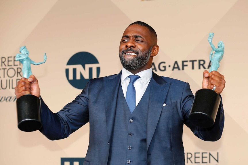 Idris Elbda holds up his two SAG awards