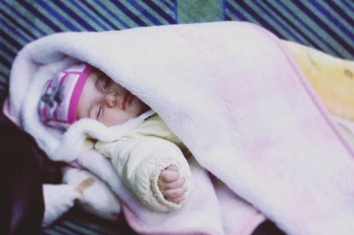 A baby lays in a train carriage wrapped in a blanket.