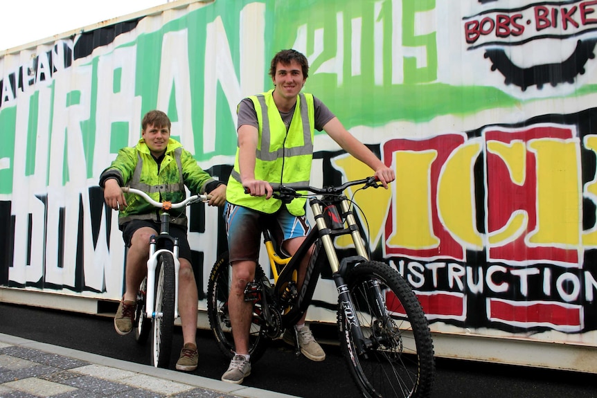 Two men with bikes stand in front of a sea container.