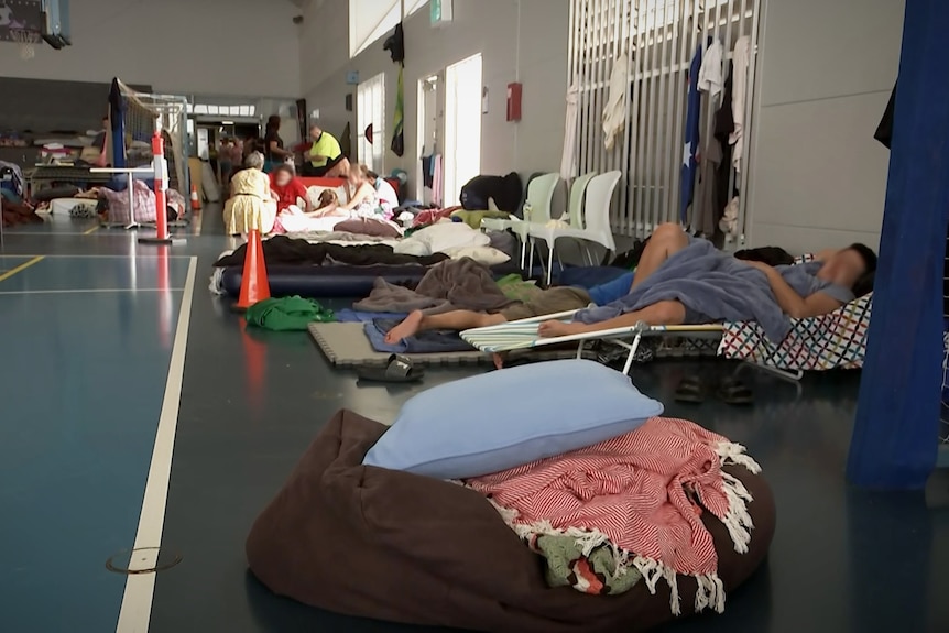 An indoor basketball court with bedding, people and belongings