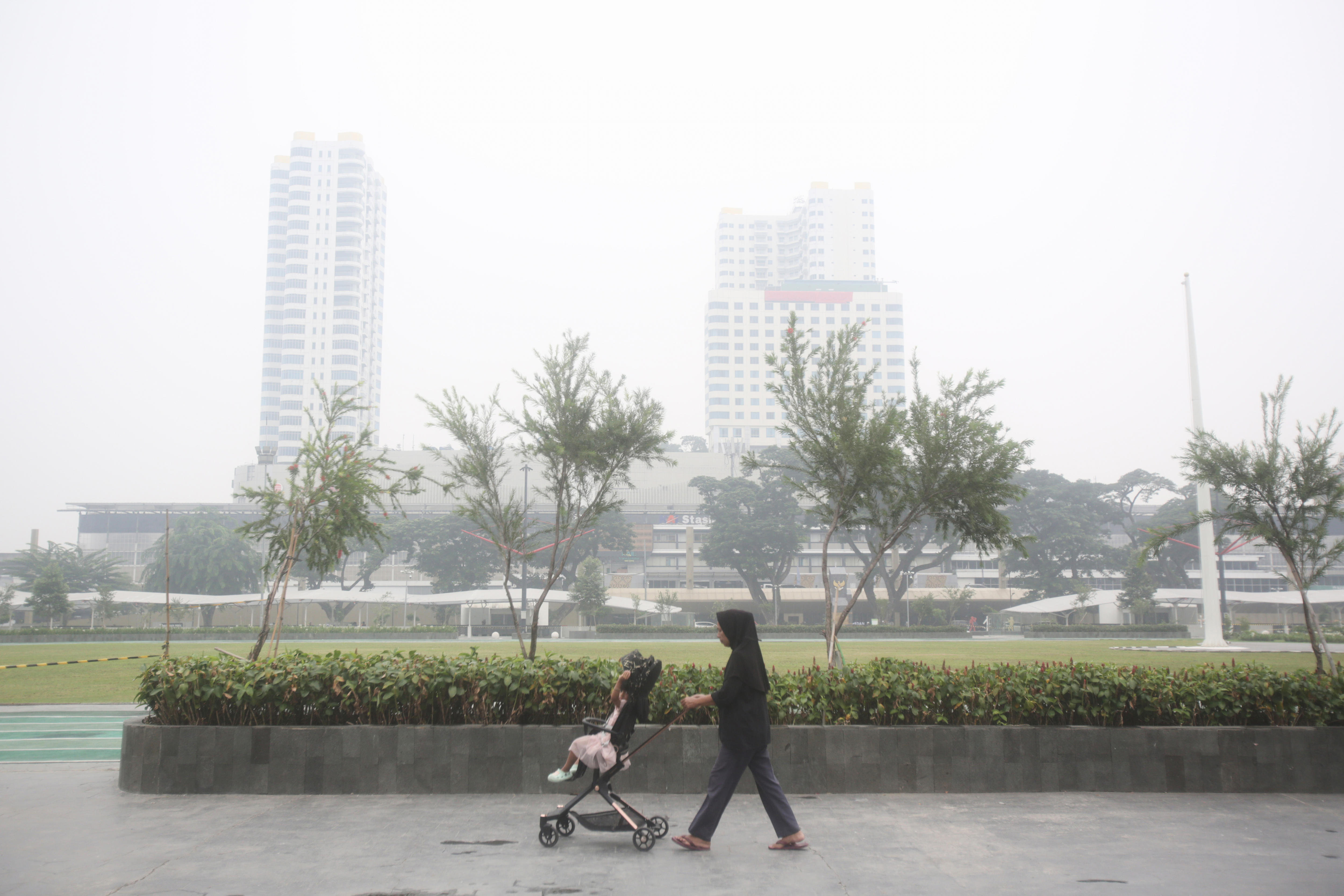 A woman pushes a stroller through a smokey cityscape 