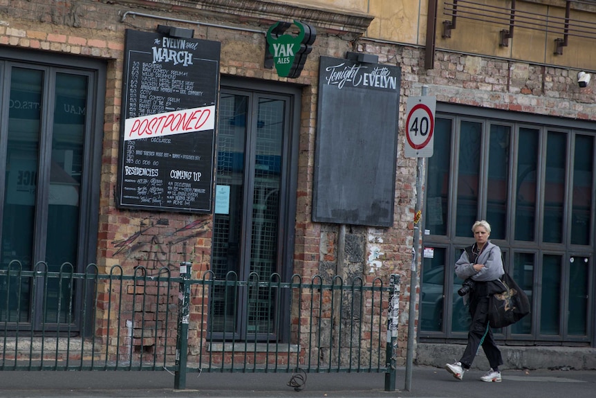 A person walks pasted a blackboard gig guide, which has "postponed" written across it, outside a hotel.