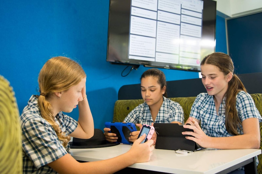 Students sit in a lounge room styled booth completing their school work on hand-held tablets.