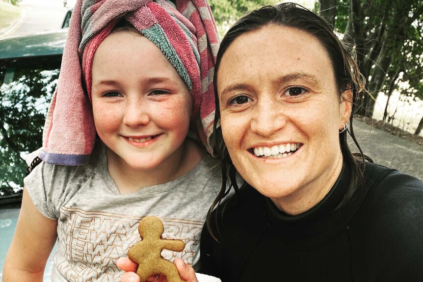 A woman and child smile as the woman holds up a gingerbread surfer-girl for a story about surf therapy helping autistic children