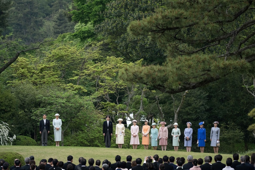 Japan's royal family presents themselves in a line, wearing formal kit while standing in a large garden.