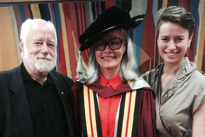 Adams standing next to Newell wearing academic gown and hat and daughter on her other side.