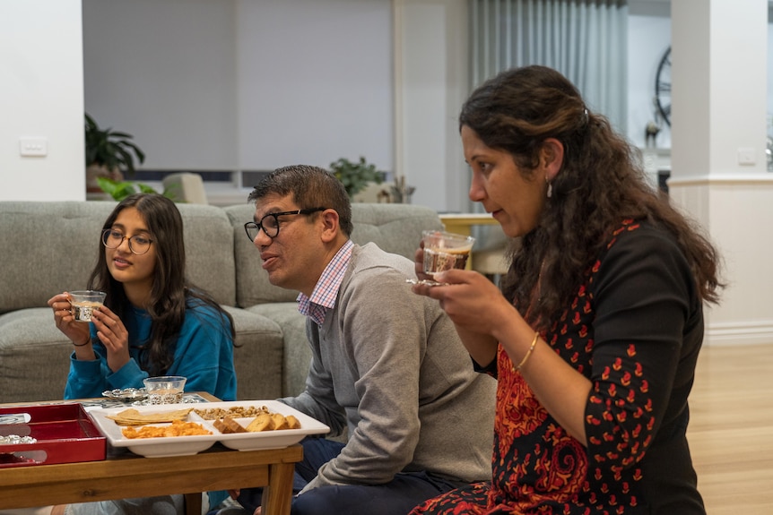 A daughter husband and wife drink tea at a table. 