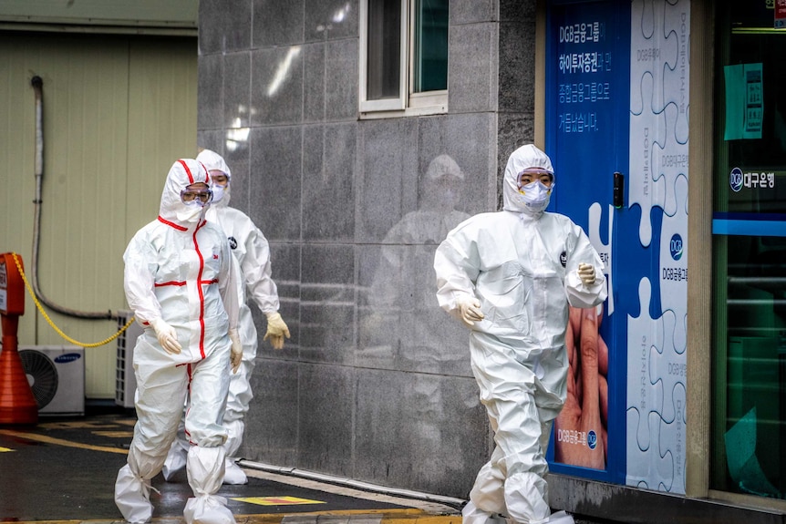 Three women in hazmat gear entering a hospital