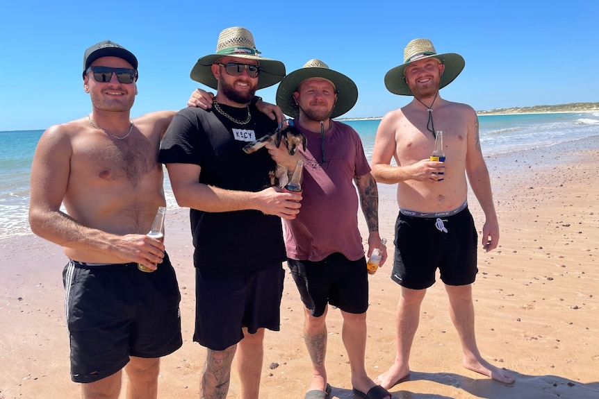 Four men at a beach with a goat.