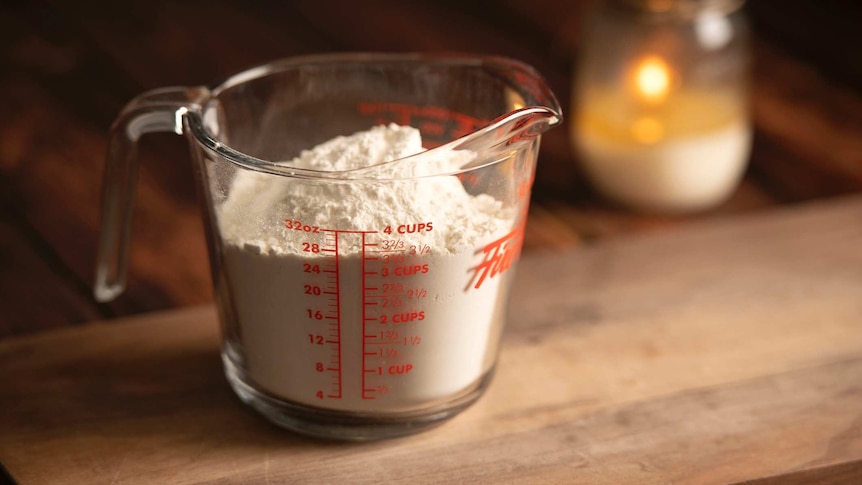A glass measuring cup sits full of flour in this still life image.