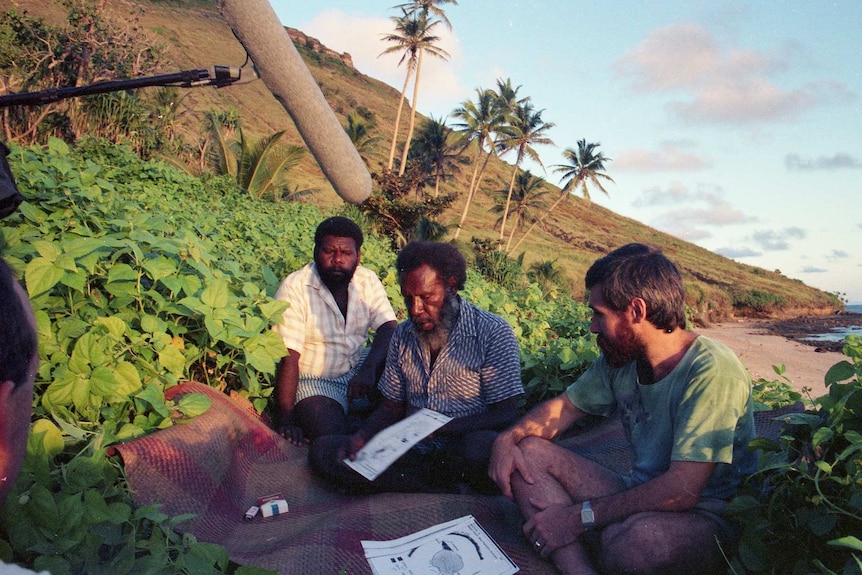 A historic photo showing Koiki Mabo, Greg McIntyre and Eddie Mabo Jnr sitting near the ocean, being interviewed.