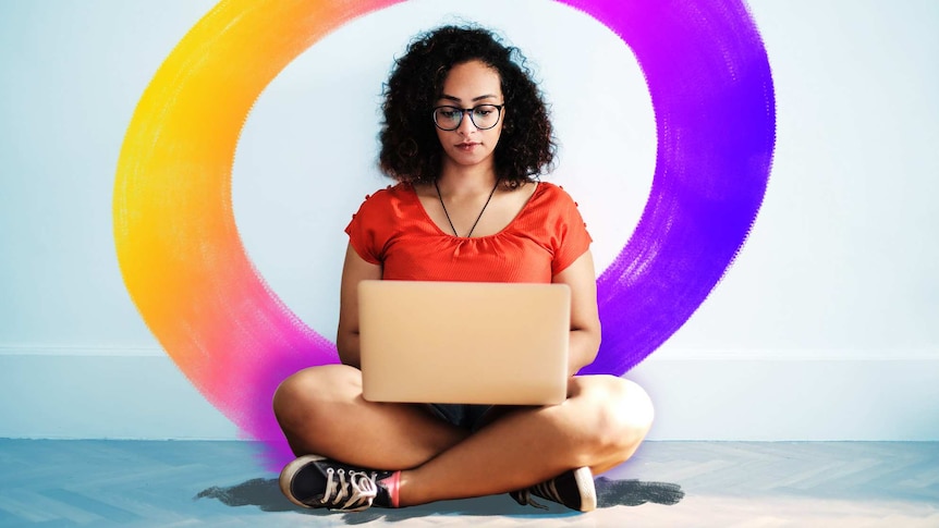 A woman sits on a floor while looking at a laptop.