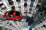 View down a deep cylindrical shaft of parked cars as a machine lifts a red VW Beetle lifted into place.