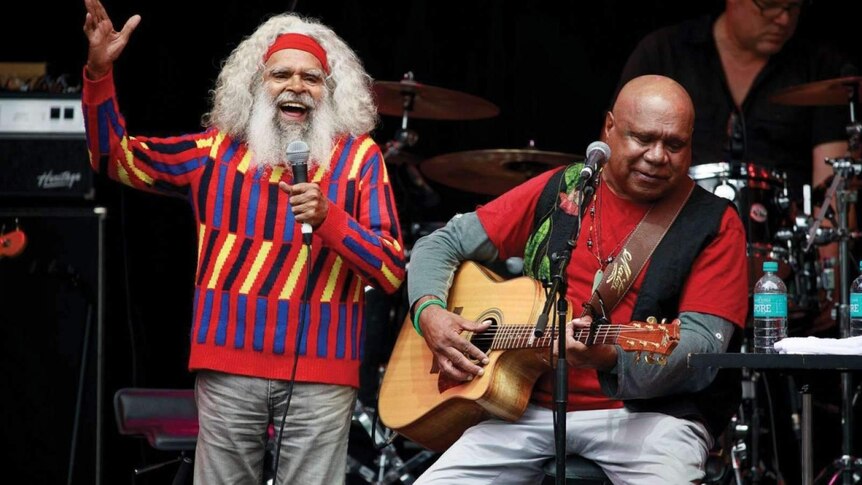 Two older Indigenous men sing and play guitar.