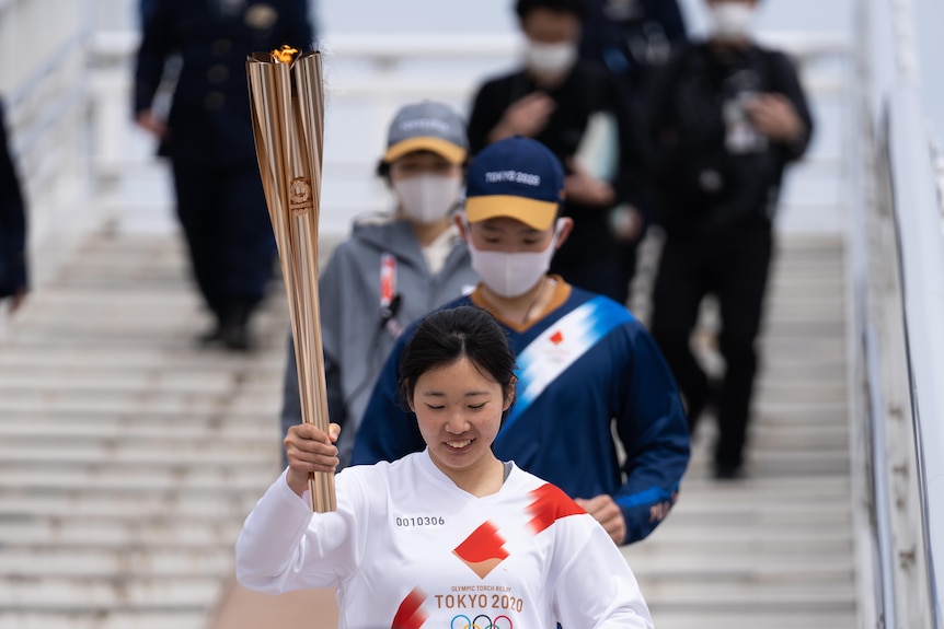 Japanese woman holding the Olympic torch with two people running behind her. 