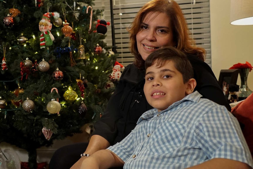 A woman and her son pose for a photo in front of a Christmas tree
