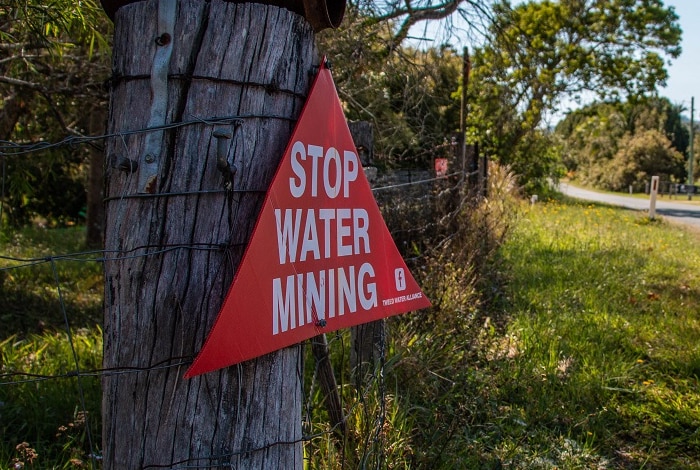 a red sign reading 'stop water mining' is nailed to an old wooden fencepost.