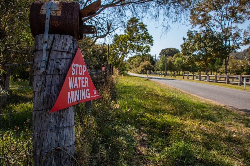 a red sign reading 'stop water mining' is nailed to an old wooden fencepost.