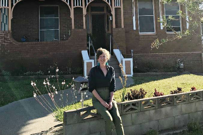 Lady sits on a fence outside a red brick 1900s home.