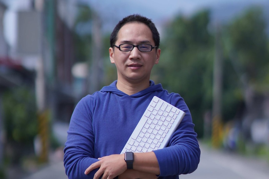 A Taiwanese man stand in an outdoor space and hold a keyboard.