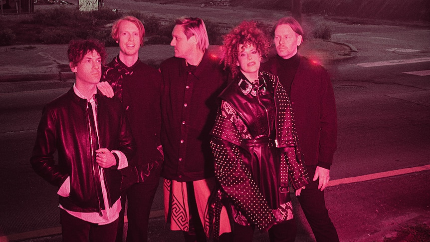 Five members of Arcade Fire stand on a deserted street, bathed in red light