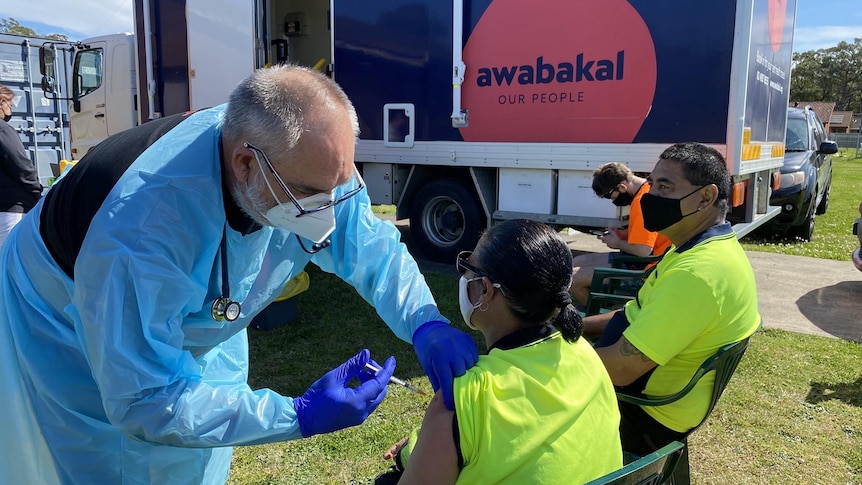 A man in protective gear injects a vaccine into the arm of an Aboriginal woman.