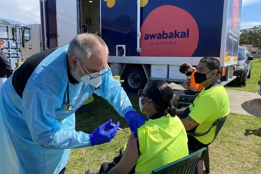 A man in protective gear injects a vaccine into the arm of an Aboriginal woman.