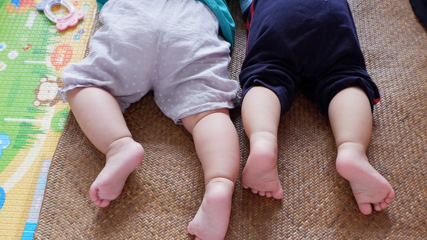 two babies can be seen lying on their tummies with bottoms facing the camera
