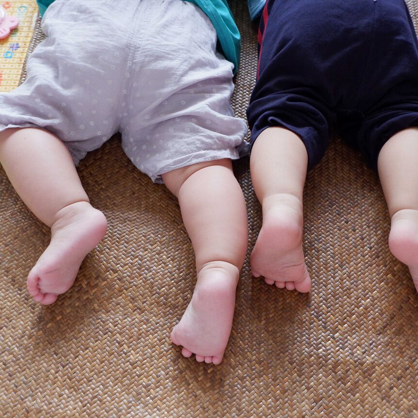 two babies can be seen lying on their tummies with bottoms facing the camera