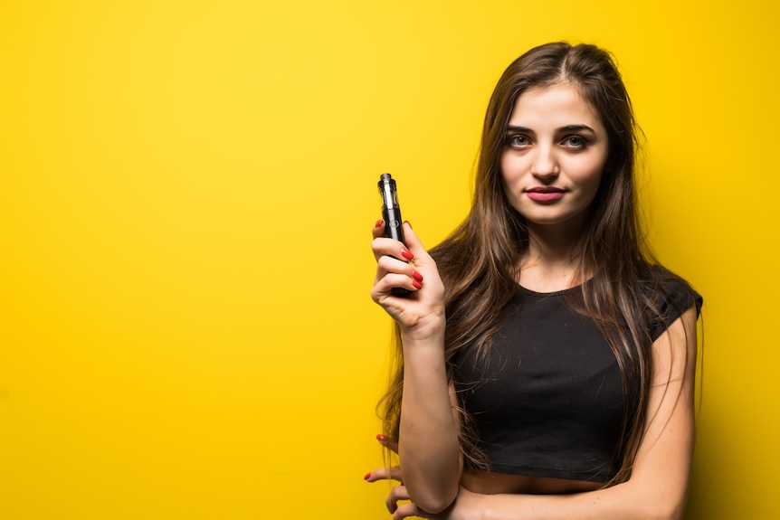 A young woman holding a vape against a yellow background