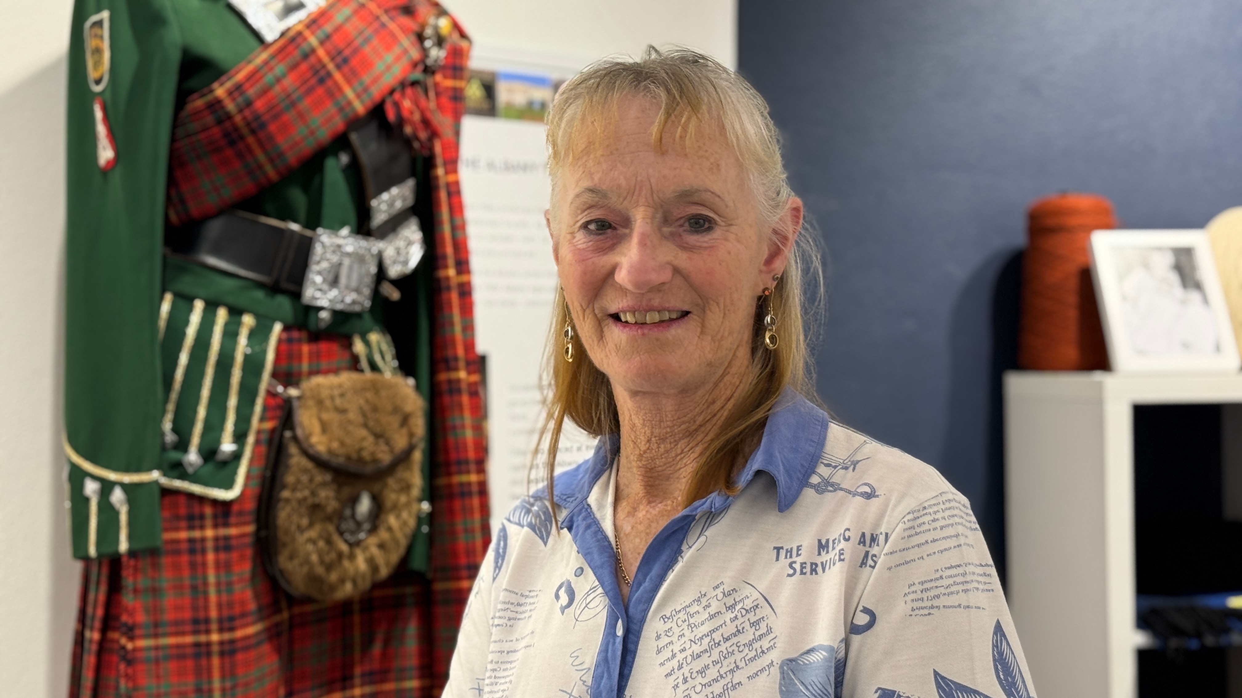 Una señora se para frente al uniforme de una banda de gaitas.