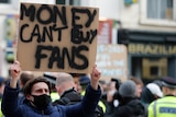 A young male holds up a sign that reaeds "MONEY CAN'T BUY FANS".