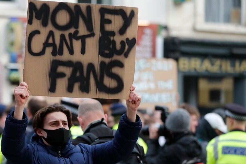 A young male holds up a sign that reaeds "MONEY CAN'T BUY FANS".
