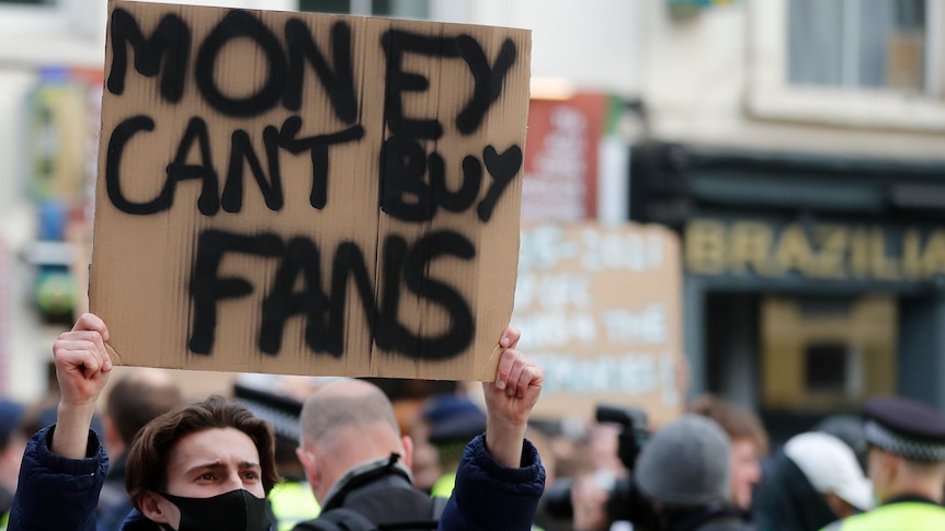 A young male holds up a sign that reaeds "MONEY CAN'T BUY FANS".