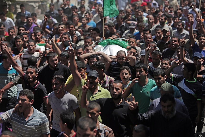 A crowd of people hold up the body of a man as they chant angry slogans.