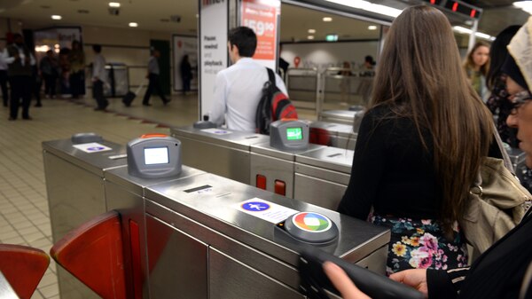 commuters at a rail station about to tap their opal card at a reader