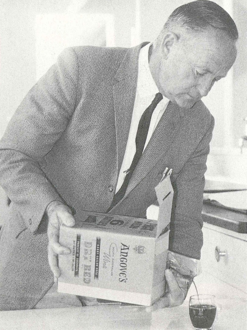 In an old photo, a man pours a glass of wine from an early version of the cask