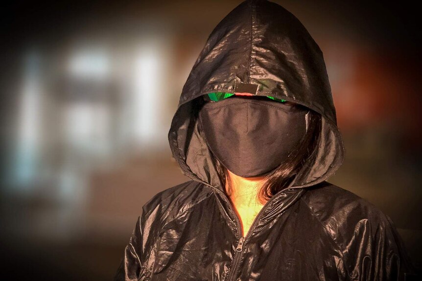 A woman in a facemask, sunglasses and black hooded jacket