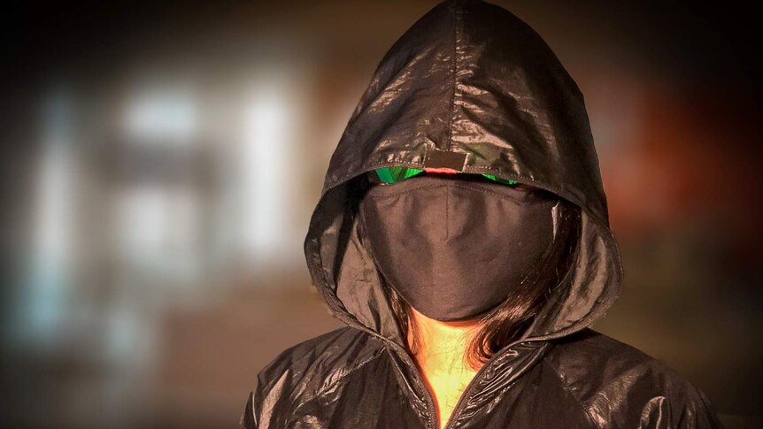A woman in a facemask, sunglasses and black hooded jacket