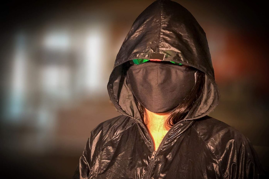 A woman in a facemask, sunglasses and black hooded jacket