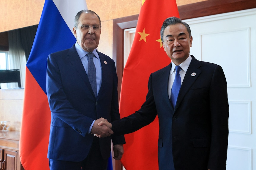 Sergei Lavrov shakes hands with Wang Yi in front of the Russian and Chinese flags while facing the camera