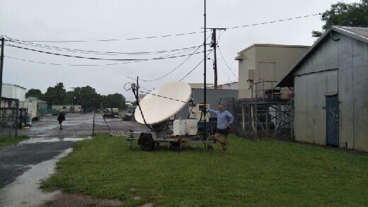 A Telstra technician stands next to a portable satellite in Daly River.