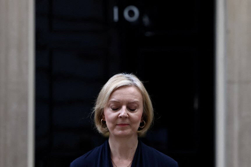 Liz Truss closes her eyes as she announces her resignation outside a black door with the number 10 on it.